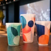 Três copos personalizados com grafismos coloridos em um evento corporativo