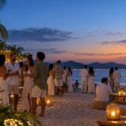 Convidados celebram o Réveillon em uma festa à beira-mar ao anoitecer, com copos reutilizáveis nas mãos.